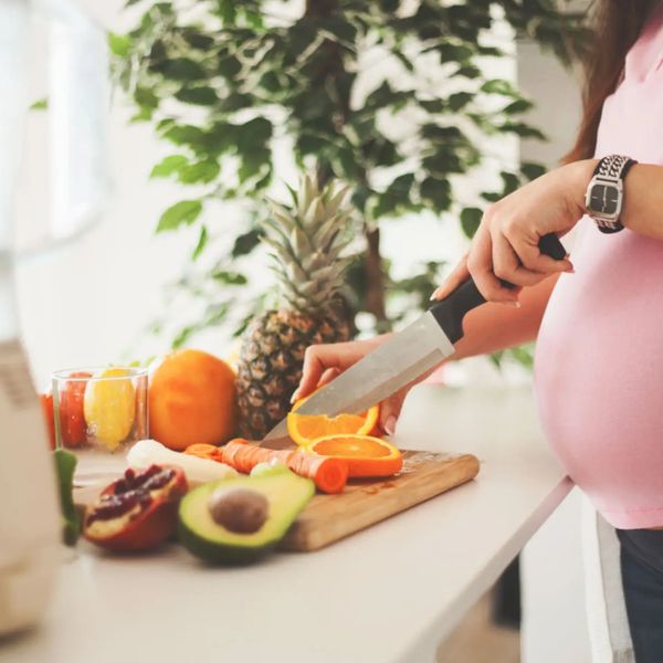 Pregnant woman slicing orange on cutting board.