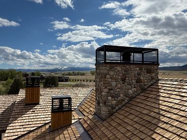 Stone chimneys on a shingled roof under a cloudy sky.