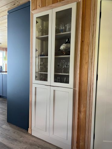 Tall white cabinet with glass doors displaying glassware and a decorative bird.
