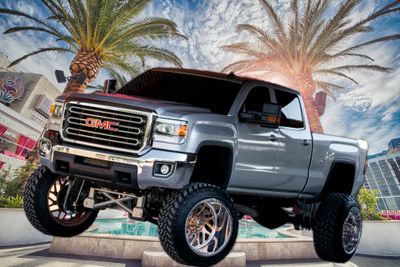 Silver GMC pickup truck with lifted suspension and large wheels under palm trees.
