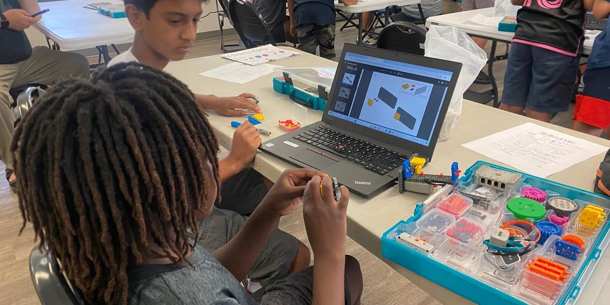 Two boys working on a robotics project using a laptop and a robotics kit.