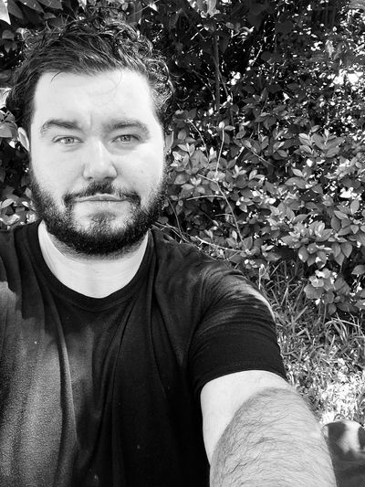 Man with beard taking a selfie outdoors.