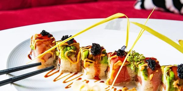 Elegant sushi rolls garnished with caviar and drizzled sauces on a white plate.
