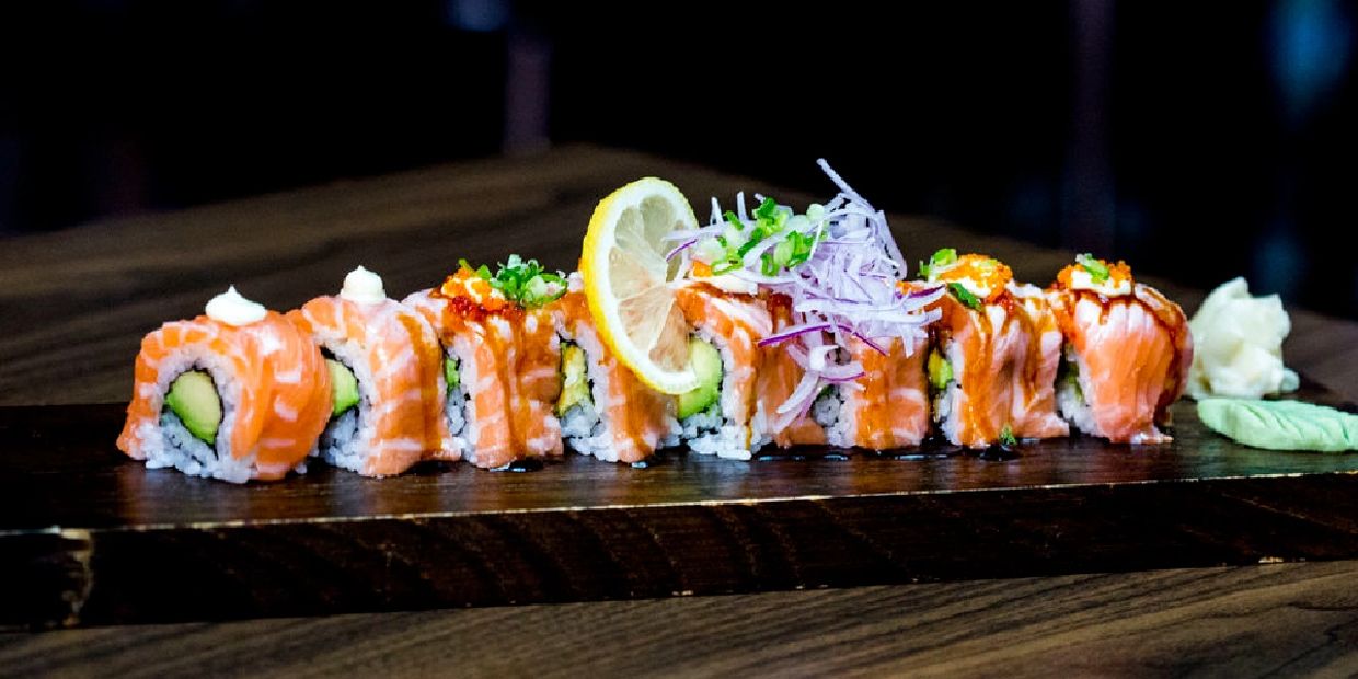 Fresh salmon sushi rolls garnished with lemon and herbs on a wooden board.