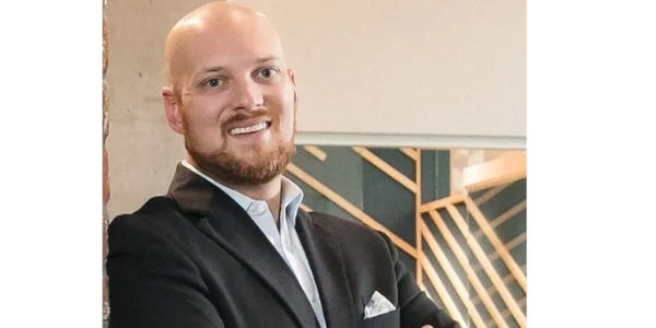 bald headed loan officer with a beard wearing a sport coat and pocket square leaning against a wall