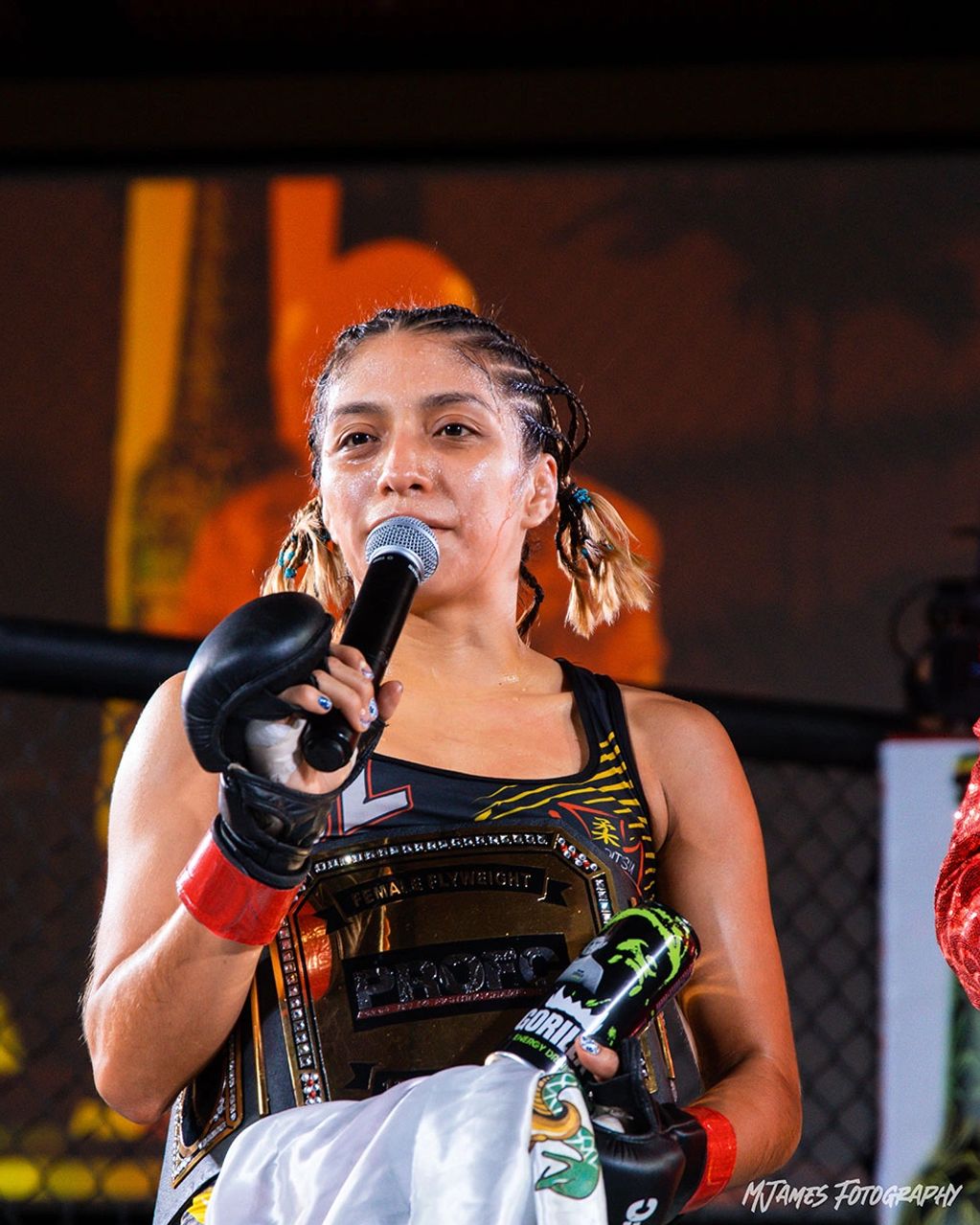 Female fighter with championship belt and microphone after a match.