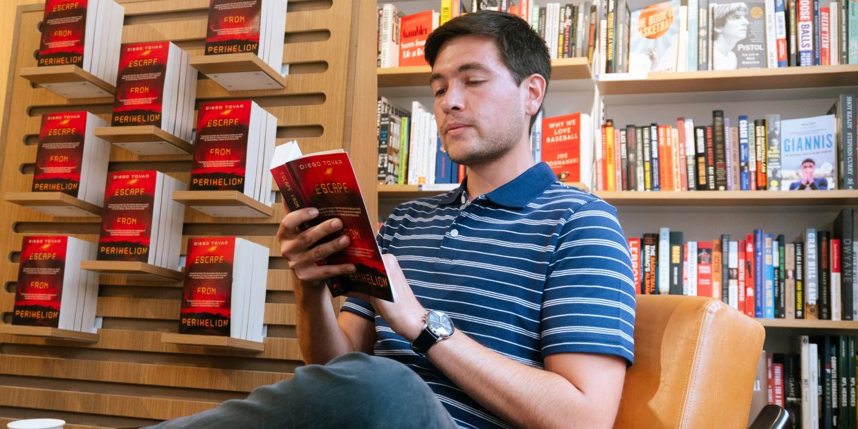 Man reading a book titled "Escape from Perihelion" in a bookstore.