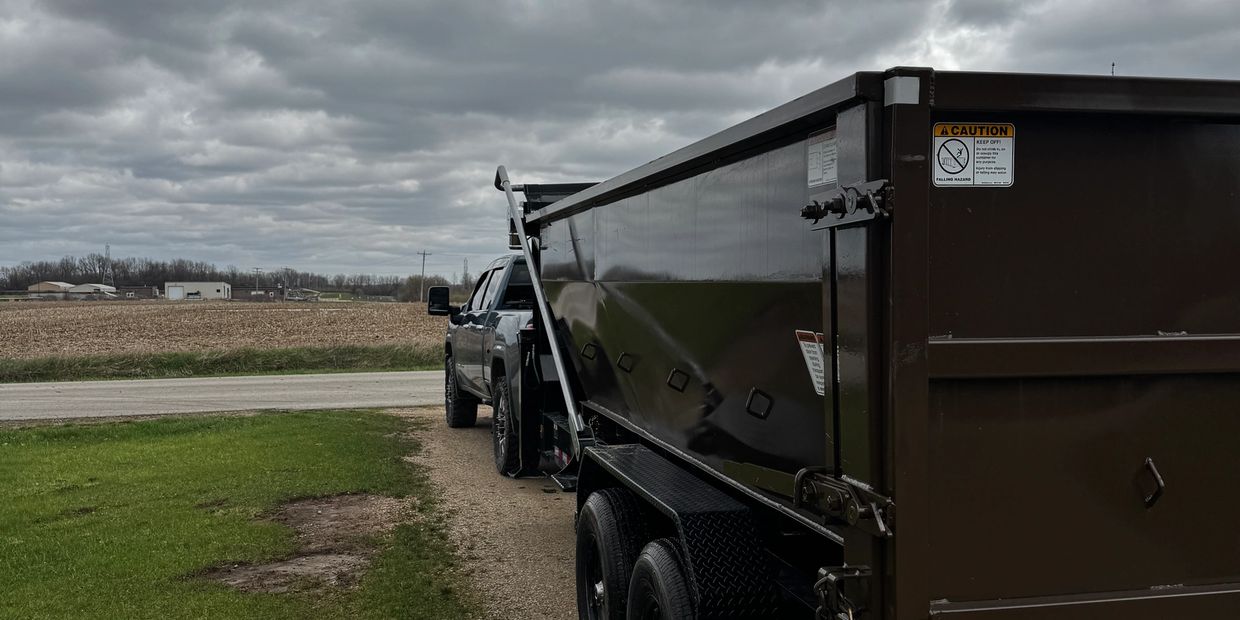 A pickup truck towing a large black trailer under a cloudy sky.