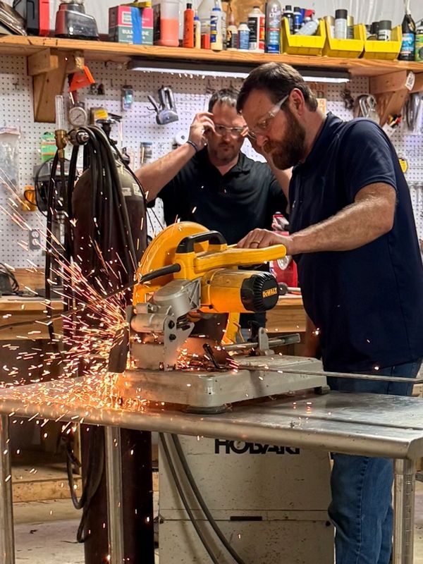 Two men using a power saw in a workshop with sparks flying.