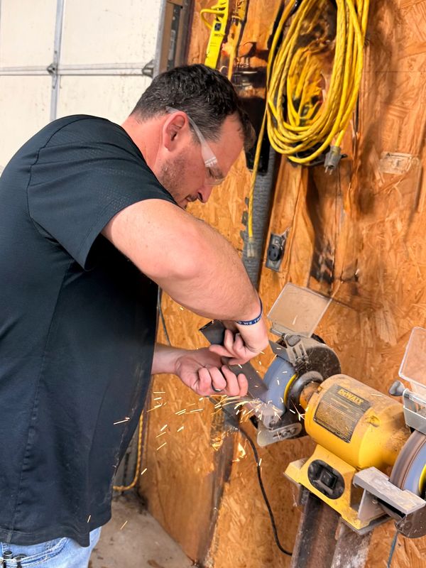 Man wearing safety glasses sharpening a tool on a bench grinder.