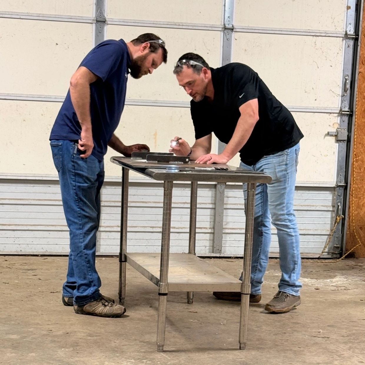Two men examining metal parts on a table in a workshop.