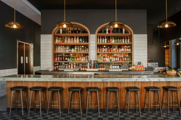 A well-stocked bar with wooden stools and pendant lights.