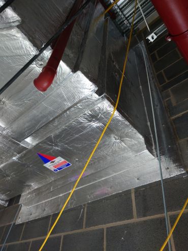Insulated ductwork and fire sprinkler pipes in a building ceiling.