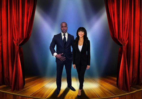 Two professionally dressed individuals stand on a spotlighted stage with red curtains.