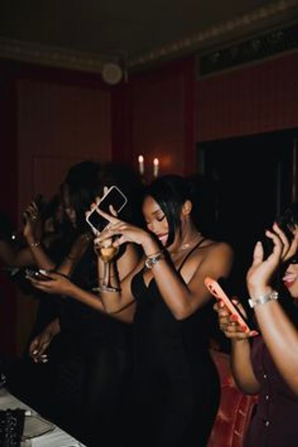 Women in elegant black dresses enjoying a night out with drinks and phones.