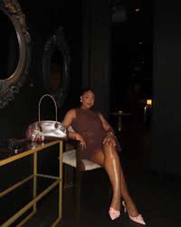 Woman in a brown dress posing elegantly in a dimly lit room.