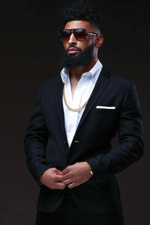 Stylish man in black suit with gold chain and sunglasses.