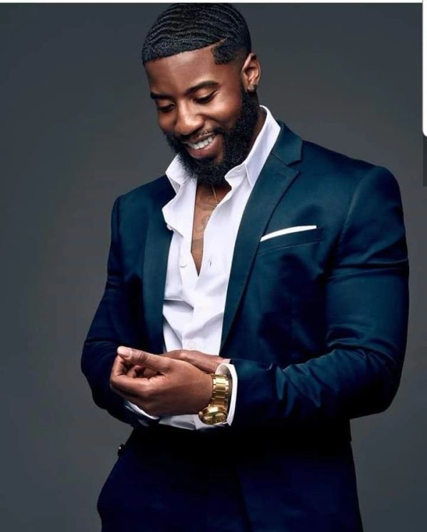 Confident man in a navy suit adjusting his cuff with a smile.