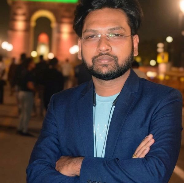 Man in a blue blazer posing with arms crossed at night.