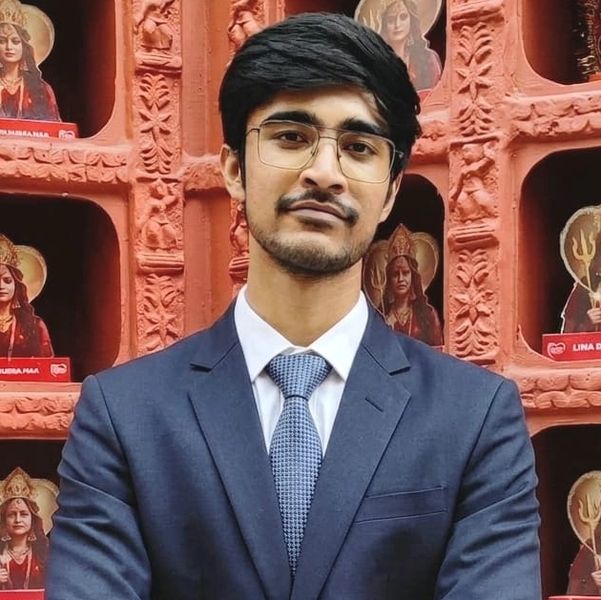 Young man in a suit poses confidently in front of a decorated wall with goddess images.