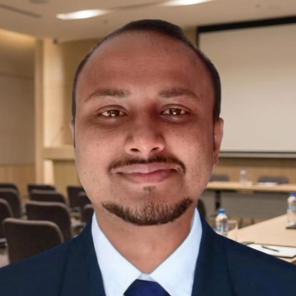 Portrait of a man in formal attire smiling in a conference room.