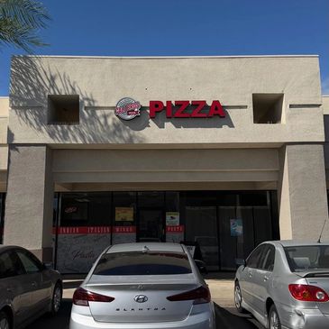 Exterior of a pizza restaurant with parked cars in front.
