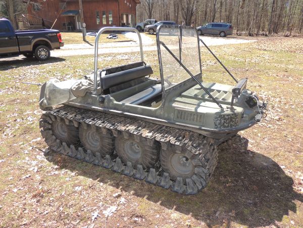 A small tracked all-terrain vehicle parked on a grassy area near a house.