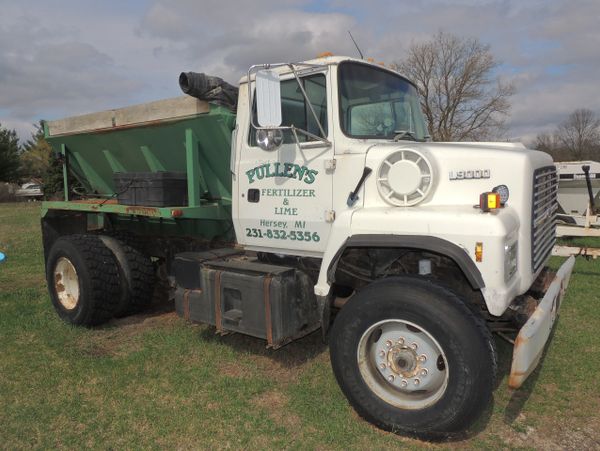 A white and green dump truck parked on grass with business signage.