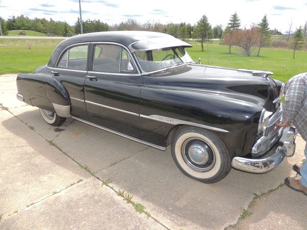 Classic black vintage car parked on a driveway under a sunny sky.