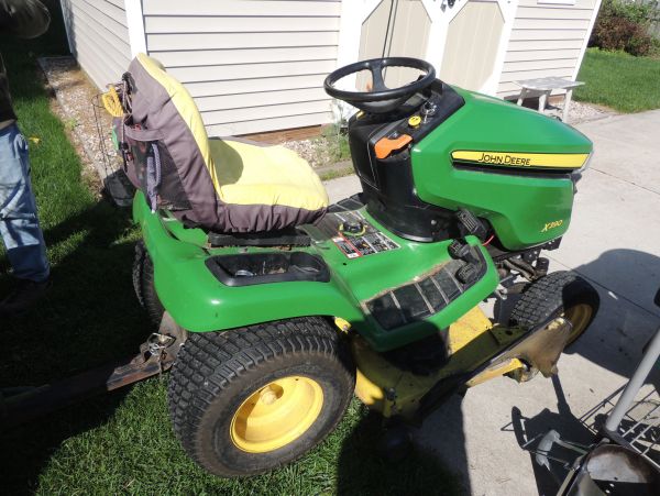 Green John Deere lawn tractor with a seat cover.