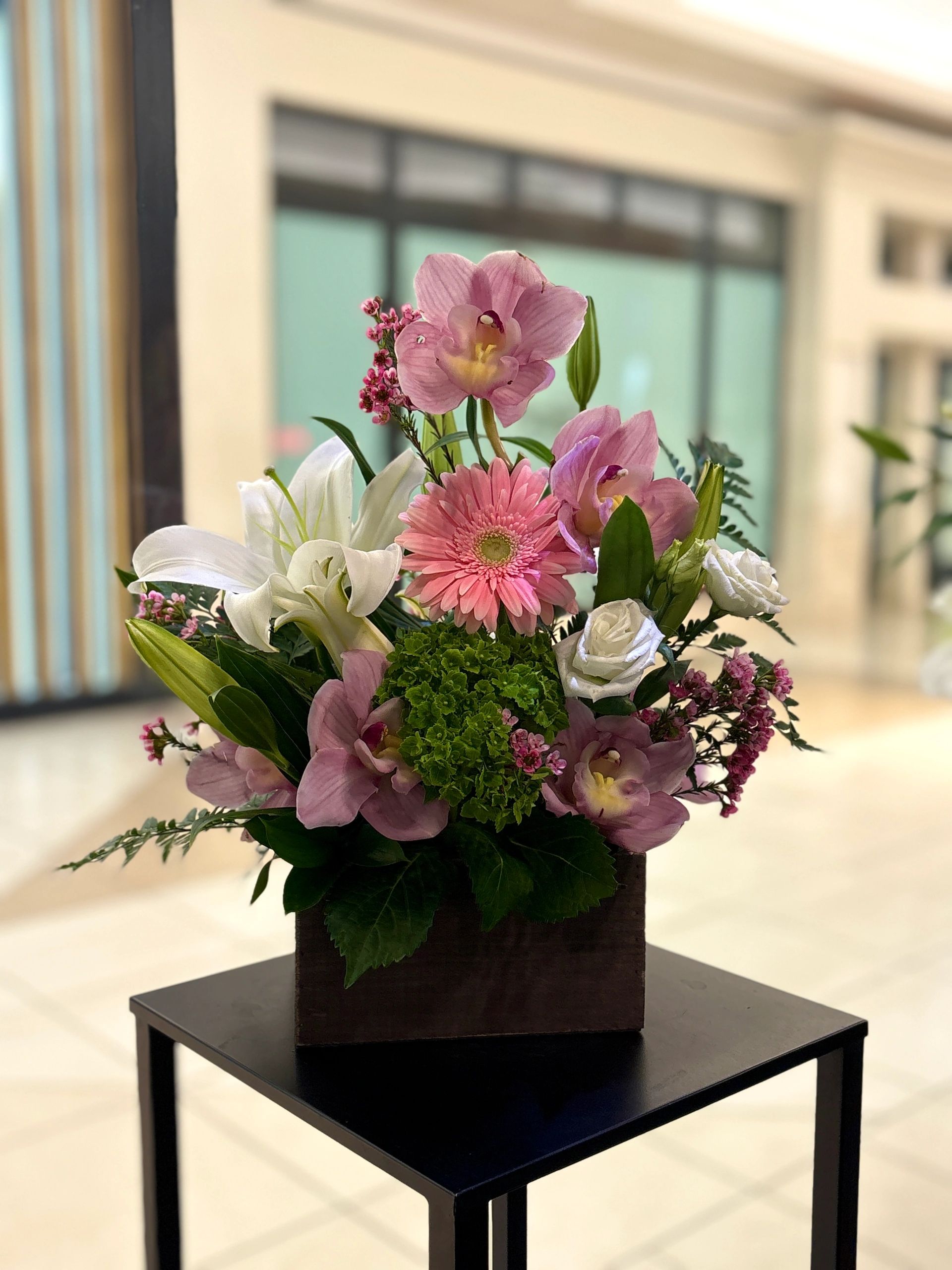 Elegant floral arrangement with pink and white flowers in a wooden vase on a black table.