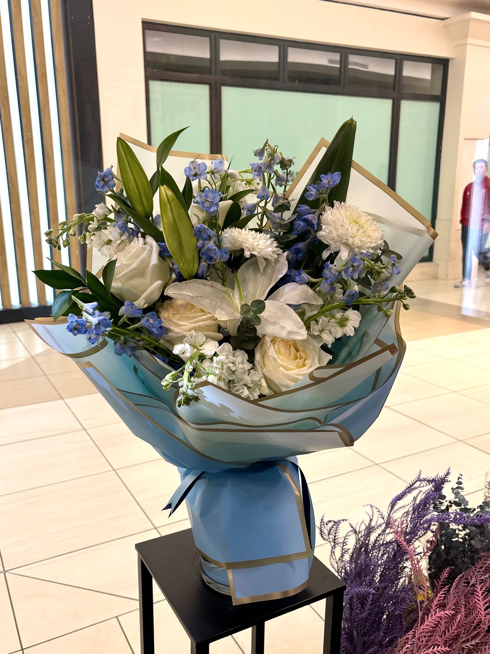 Elegant bouquet with white and blue flowers wrapped in blue paper.