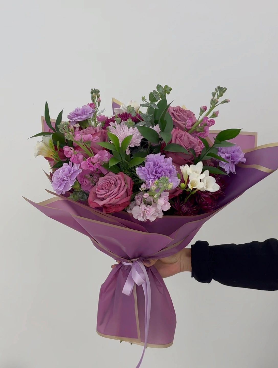 A vibrant bouquet of purple and white flowers wrapped in purple paper.