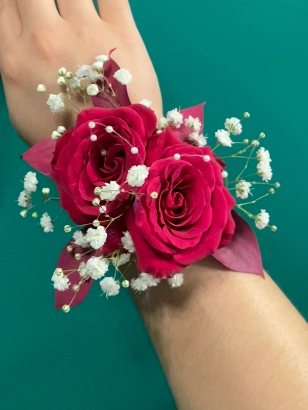 Wrist corsage with red roses and white baby's breath flowers.