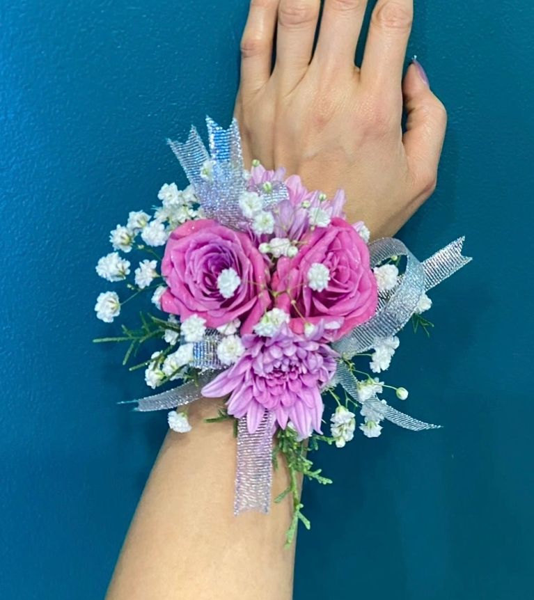 Hand adorned with a pink floral wrist corsage against a blue background.