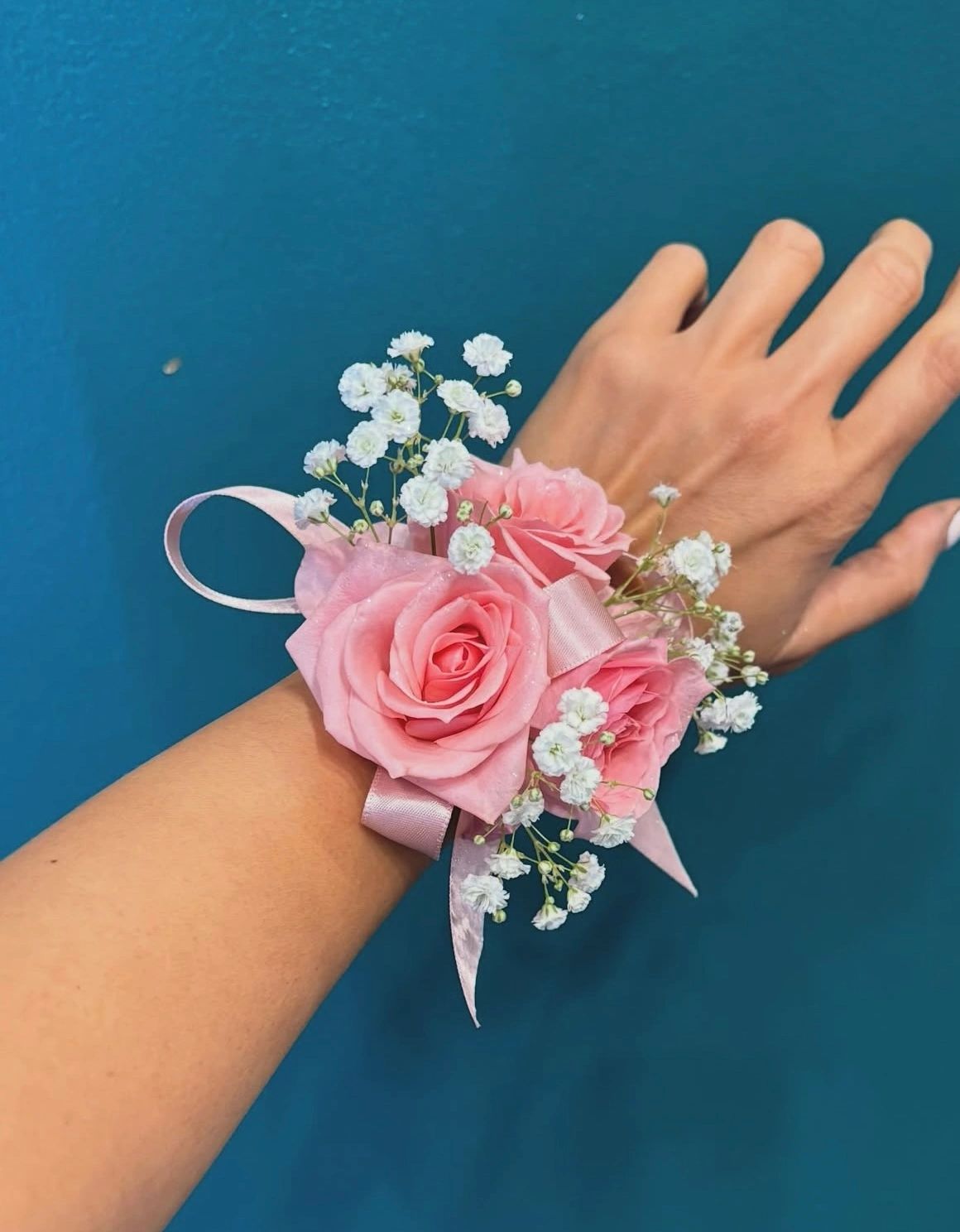 A wrist corsage with pink roses and white baby's breath flowers.