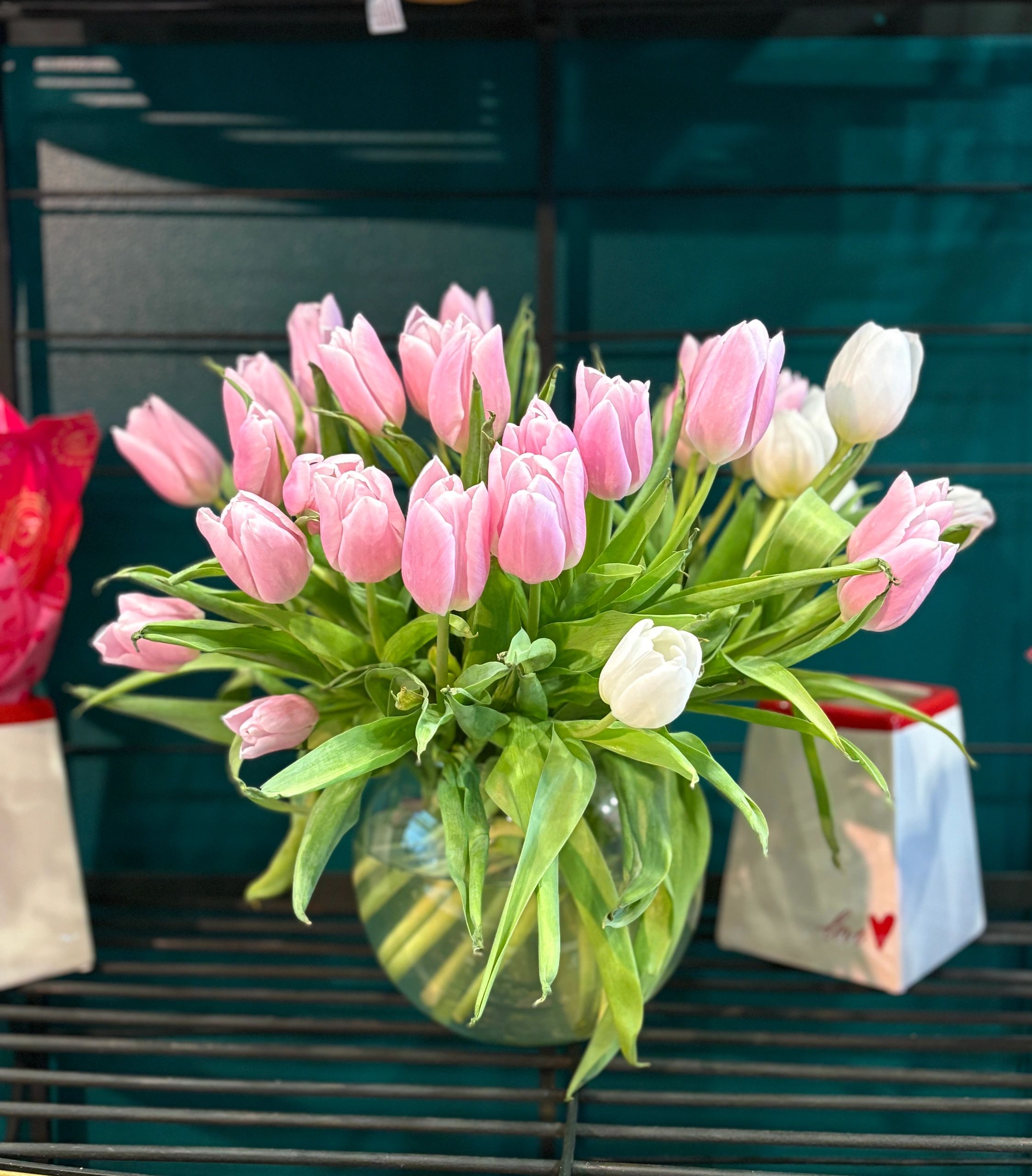 A bouquet of pink and white tulips in a glass vase on a bench.