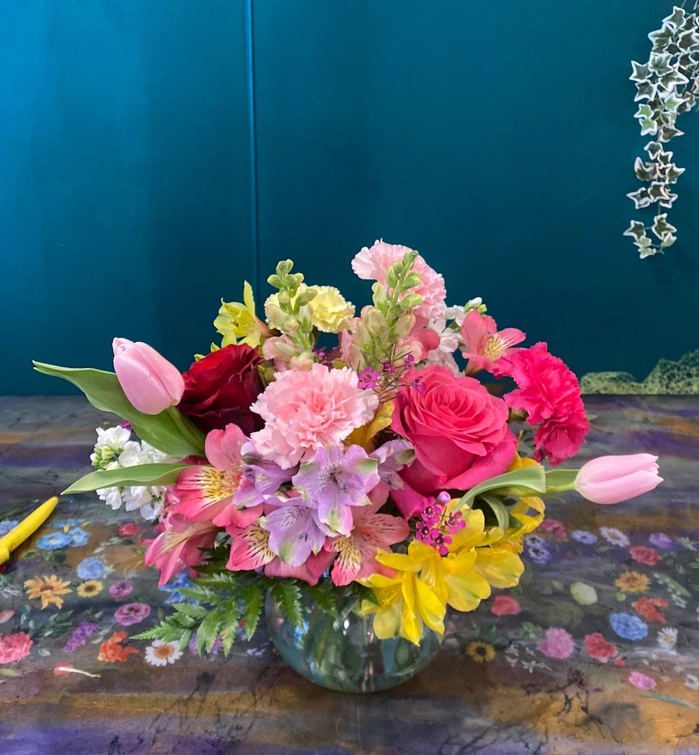Colorful flower bouquet in a clear round vase on a floral table.