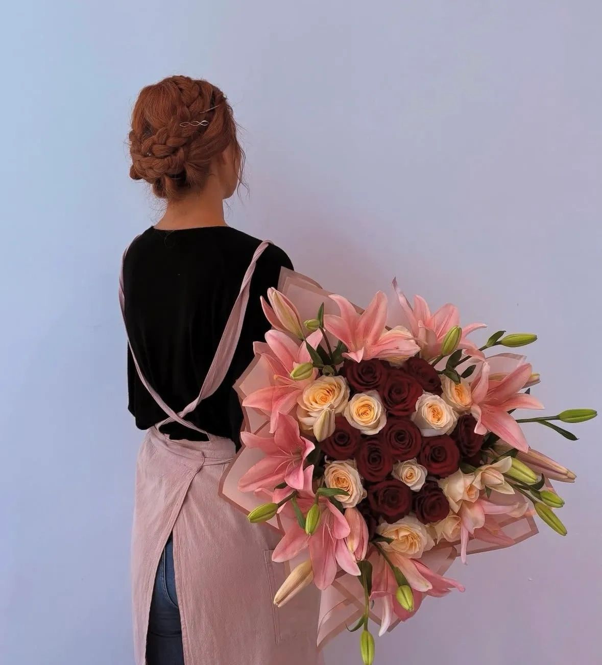 Woman with braided hair holding a large bouquet of pink lilies and roses.