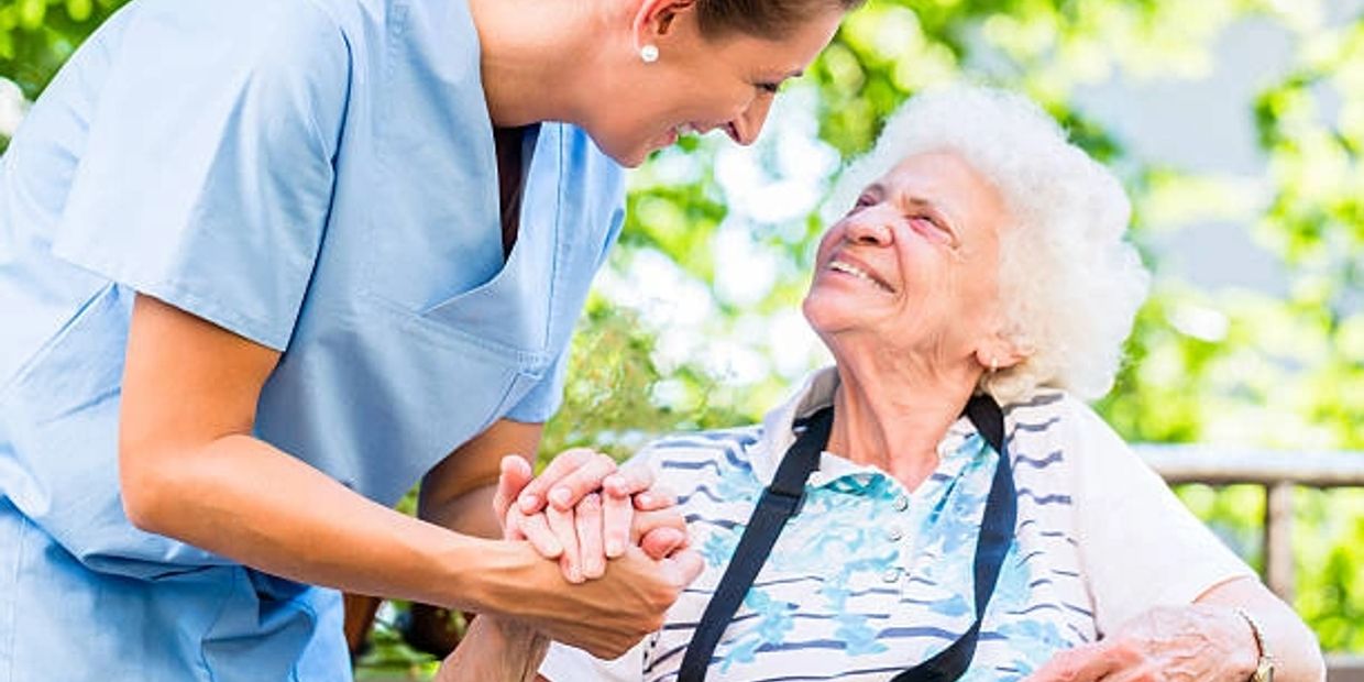 A nurse warmly holding hands and smiling at an elderly woman outdoors.