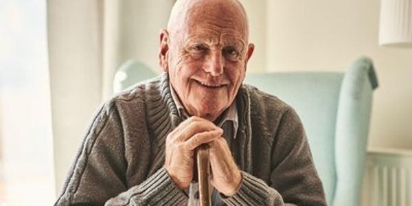 Elderly man smiling warmly while holding a cane indoors.