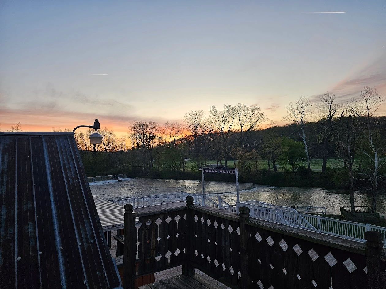Sunset over a riverside park with wooden decks and bare trees.