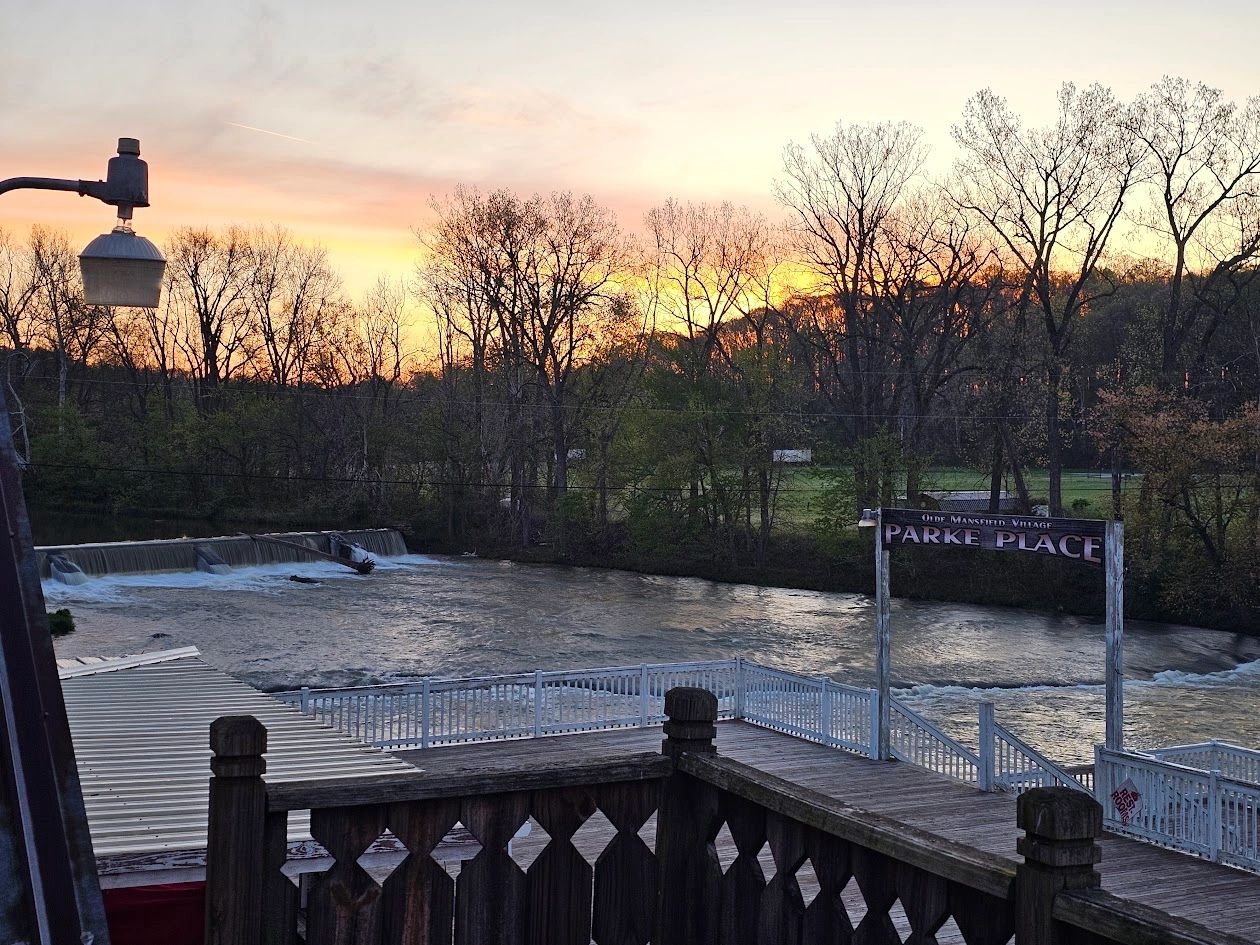 Sunset over a flowing river with a wooden deck and a Parke Place sign.