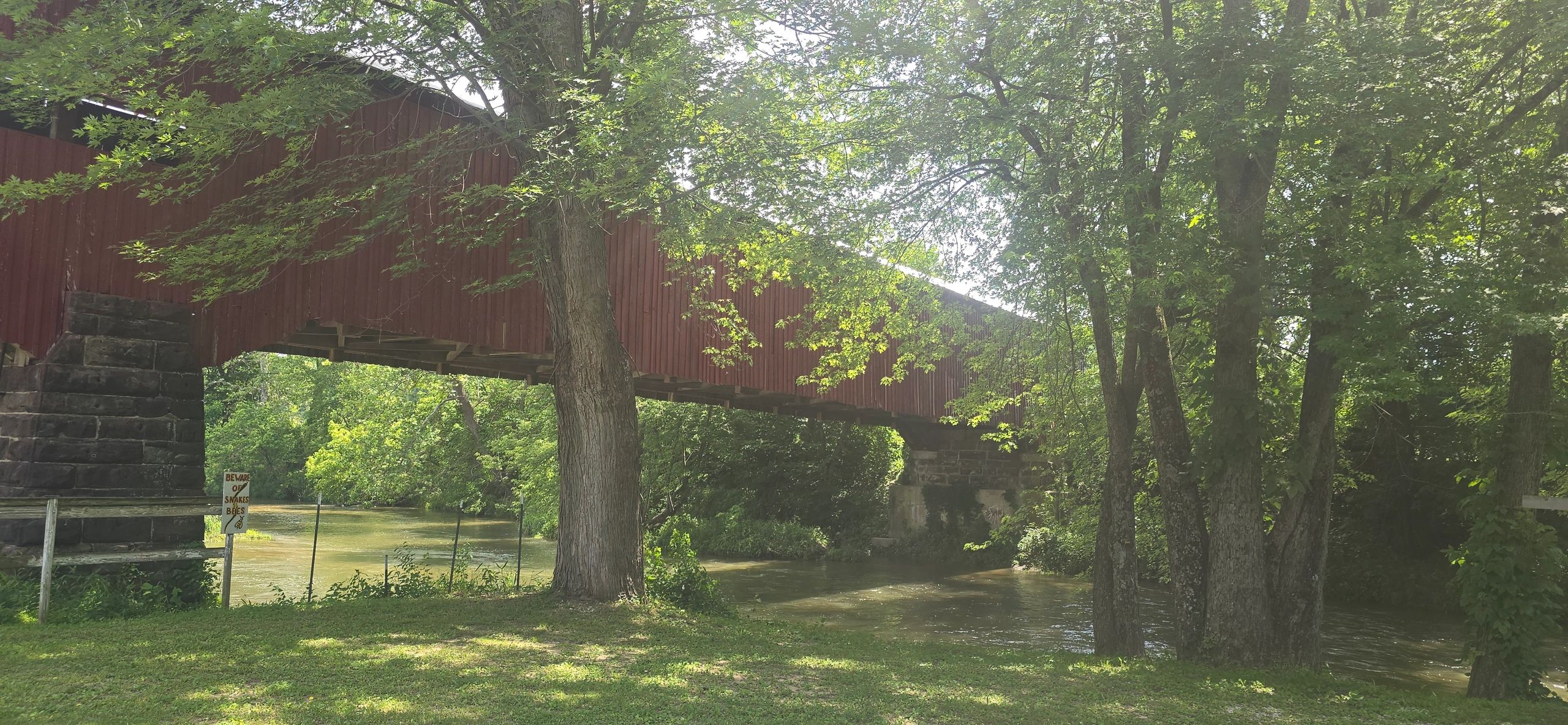 A red covered bridge over a river surrounded by lush green trees.