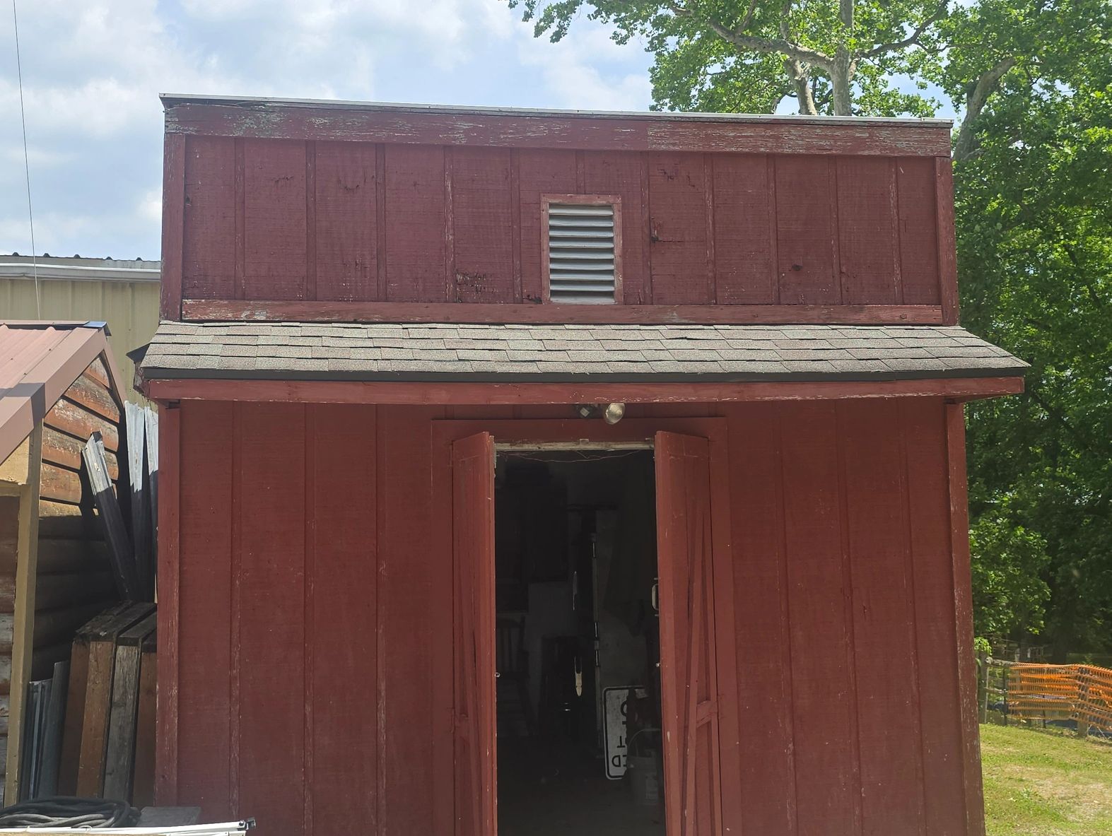 A rustic red wooden shed with open double doors and a small vent above.