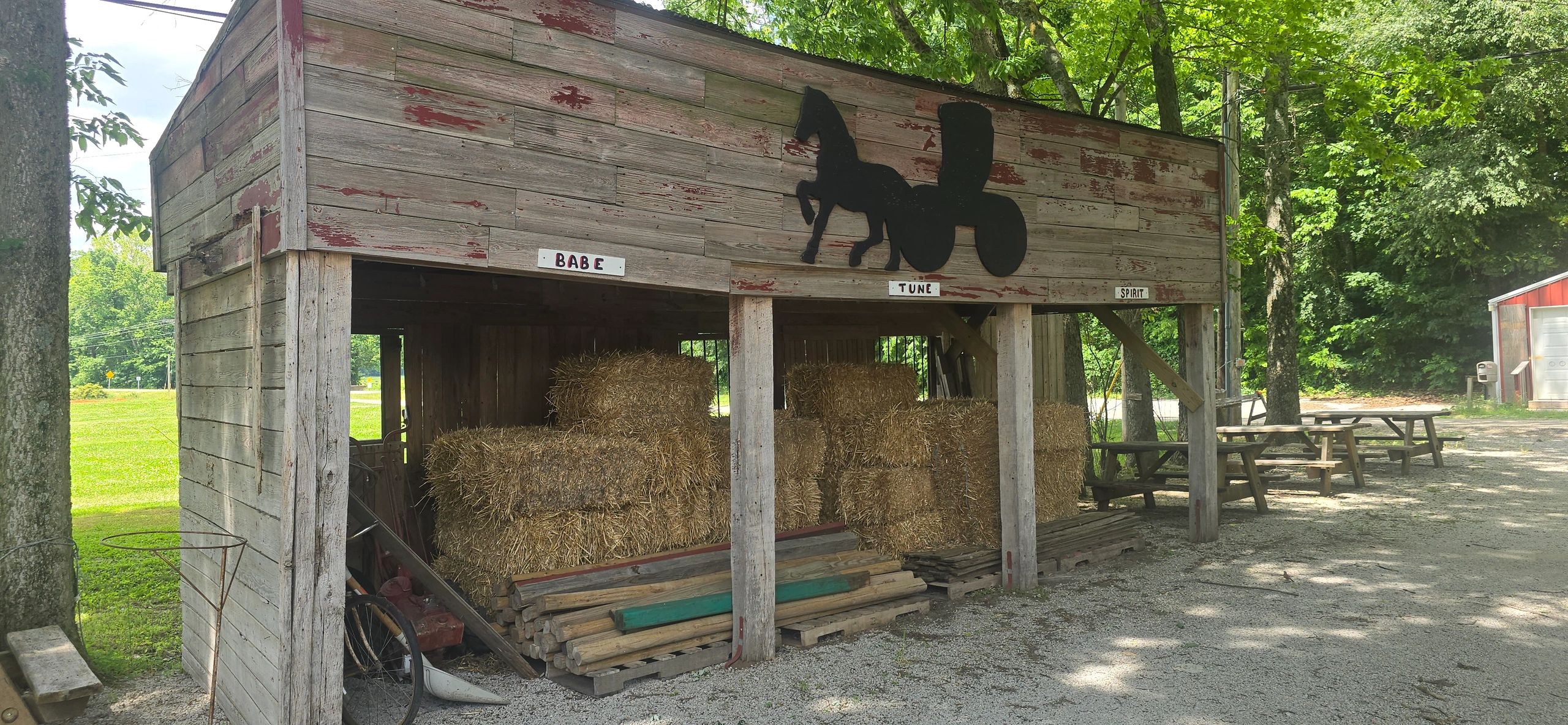 Rustic wooden barn storing hay with horse silhouettes and names above.