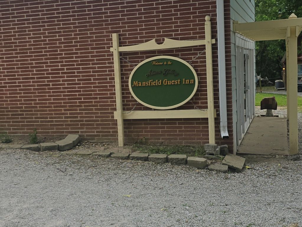 Sign for Mansfield Guest Inn on a brick wall beside a gravel driveway.
