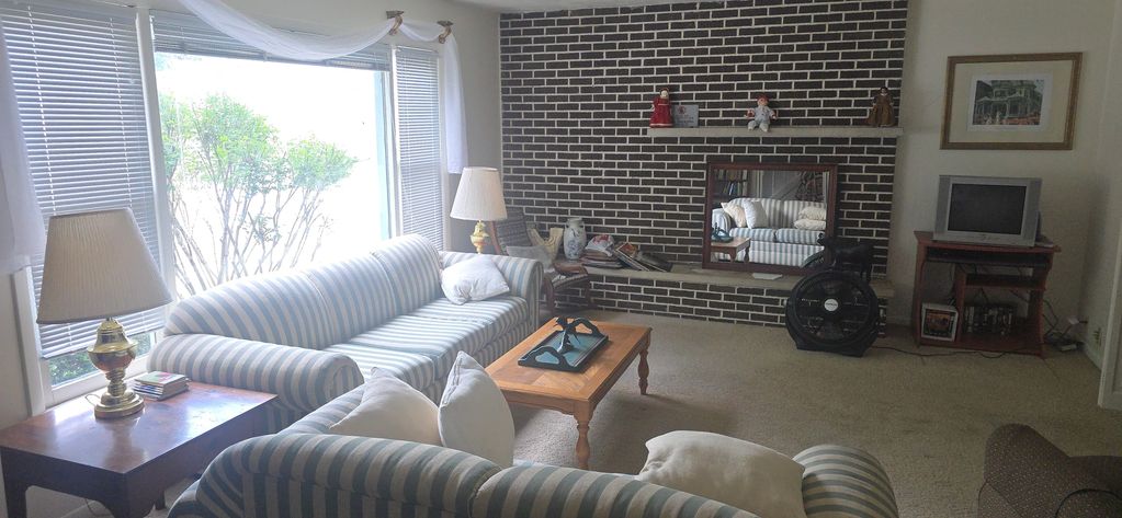 Cozy living room with striped couches, a brick fireplace, and ample natural light from large windows.