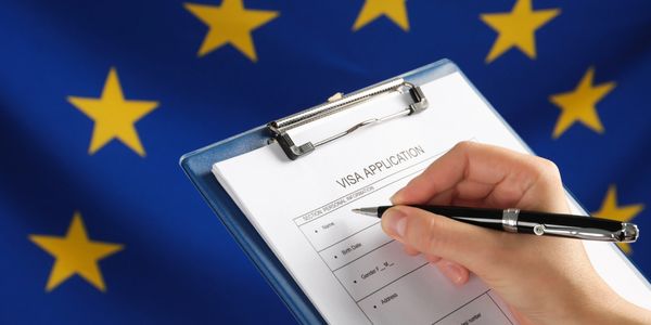 A hand filling out a Schengen visa application form with Europe's flag in the background.