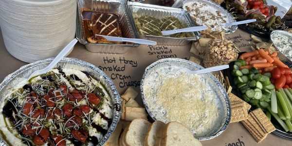 A buffet table with assorted dips, vegetables, crackers, and bread slices.